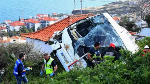 AFP Firemen stand next to the wreckage of a tourist bus that crashed in Madeira on April 17, 2019