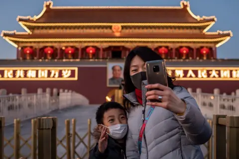 Nicolas Asfouri / AFP A woman and a boy wearing protective masks take a selfie in front of a portrait of late communist leader Mao Zedong at Tiananmen Gate in Beijing.