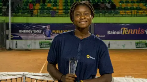 Eddy Edwards Marylove Edwards smiles holding trophy in front of net