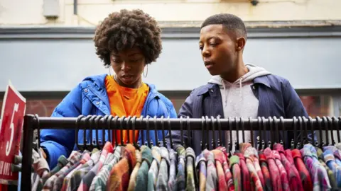Getty Images Two friends looking at a rack of clothes in a market