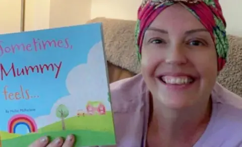 Hollie McFarlane Hollie wearing a headscarf and holding her book titled Sometimes, Mummy feels... with a smile on her face