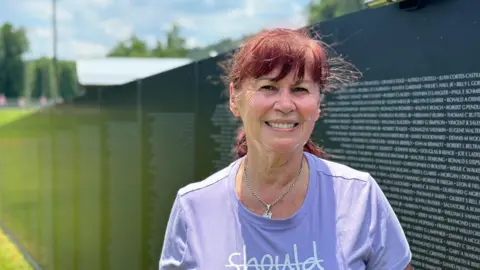 Brandon Drenon/BBC Gloria Murphy stands in front of a memorial honouring US soldiers who died in the Vietnam War 