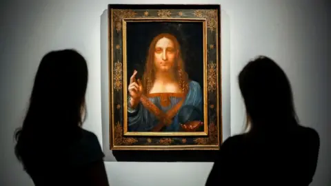 Getty Images Staff members pose next to a painting by Leonardo da Vinci entitled Salvator Mundi before it is auctioned at Christie's in New York