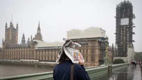 Getty Images A pedestrian holds a newspaper over their head to shelter from rain near the Palace of Westminster