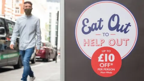 PA Media A poster for the Eat Out to Help Out scheme with someone walking in the background