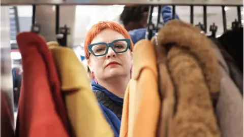 Ibi Gowon Women looks through rack of clothes in Charity Super.Mkt