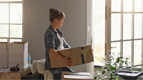 Getty Images Woman carrying boxes into home