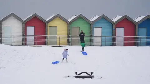 PA Media People walk through the snow beside the beach huts at Blyth in Northumberland, as temperatures are tipped to plunge to as low as minus 11C in parts of the UK over the weekend.
