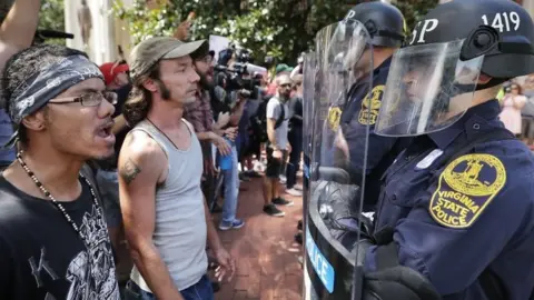 Getty Images Virginia State Police wear body armour and use riot shields while keeping crowds away from alt-right blogger Jason Kessler after he tried to hold a news conference on 13 August 2017