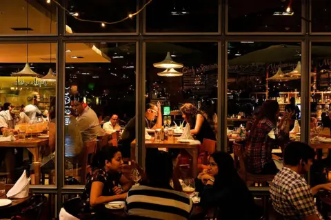Getty Images In this photograph taken on May 11, 2016, people eat food inside a restaurant in DLF Cyber City area of Gurgaon, 32 kilometres southwest of the capital New Delhi. The satellite town of Gurgaon near the Indian capital is home to scores of top multinational companies, and the influx of foreign capital has brought with it gleaming shopping malls enjoyed by India's rising middle class seeking an outlet for their disposable income