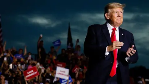 Getty Images Donald Trump claps as a crowd of supporters cheer behind him.