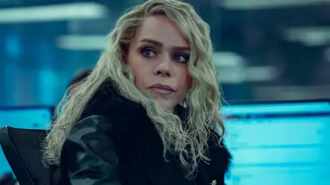 BBC Billie Piper wearing a black leather jacket. She has long blonde curly hair. 