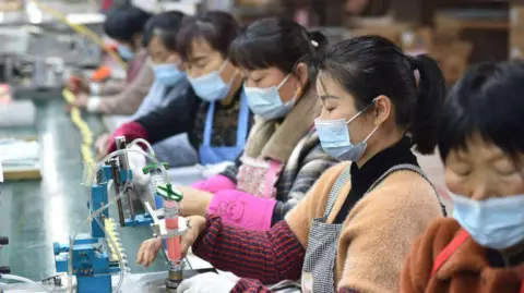 Getty Images Chinese women wearing masks assemble speakers on a production line at a Chinese electronics company