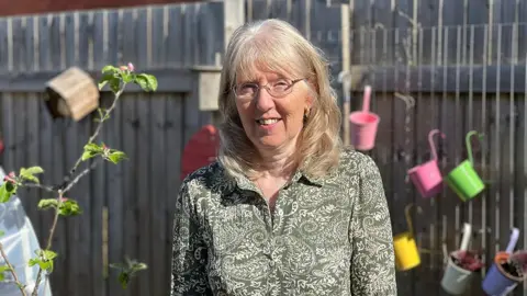 BBC / Sarah Sanderson Pamela Hodge has blond hair and glasses and wears a green floral patterned shirt