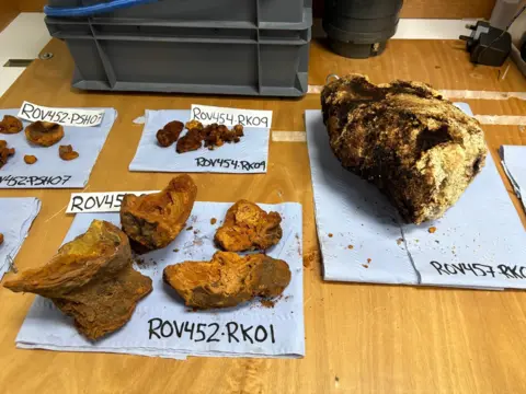 A table with pieces of orange, yellow and black volcanic rock laid out on top of blue paper with labels written on them.