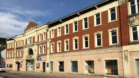Andrew Poole An old cinema building with a brick faced and the name Pavilion above the entrance with a blue sky overhead