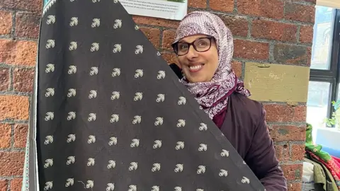 Yorkshire Women's Forum A smiling woman, wearing a headscarf, holds up a large piece of patterned black material