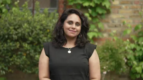 Anu Chandrasekar in a black T-shirt. She has brown hair and wears colourful earrings. 