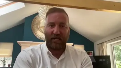 UGC Mr El Paraiso, who has a beard and is wearing a white shirt, sits looking at the camera on a Zoom call with leaseholders that took place in June 2024