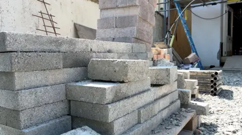 BBC A stack of grey bricks on a pallet at a building site.