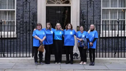 PA Media Six women wear blue T-shirts and stand arm-in-arm outside Number 10 Downing Street. They are all straight-faced.
Pictured in the image left to right are: Joanna Alkir, Crystal Owen, Alison Greenhouse, Nicola Bell, Bridget Lucas and Naomi Crane.