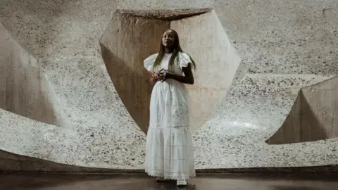 AFP/Getty Images Wearing a long, white dress, Kouoh poses in front of a large, white sculpture.