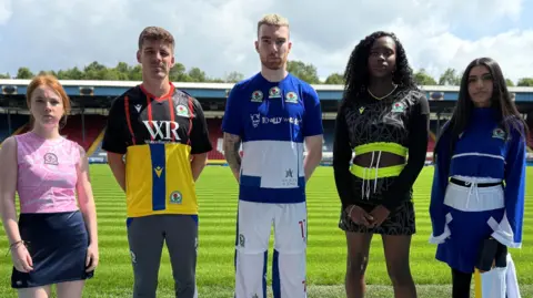 BBC Five models - three women and two men on Blackburn Rovers' pitch at Ewood Park wearing recycled football kits.