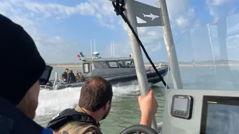 Marianne Baisnée/BBC Two men sit in the patrol boat, with a second patrol boat on the water across from them