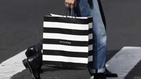 Getty Images Image shows a black and white striped bag held by a woman walking across a zebra crossing. You can only see her bottom half - she is wearing jeans and black ankle boots and someone is behind her taking the same step. 