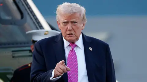Getty Images US President Donald Trump walks to Air Force One at Morristown Airport on 14 September. He is pictured in a navy suit and a pink patterned tie while pointing his finger towards the camera.